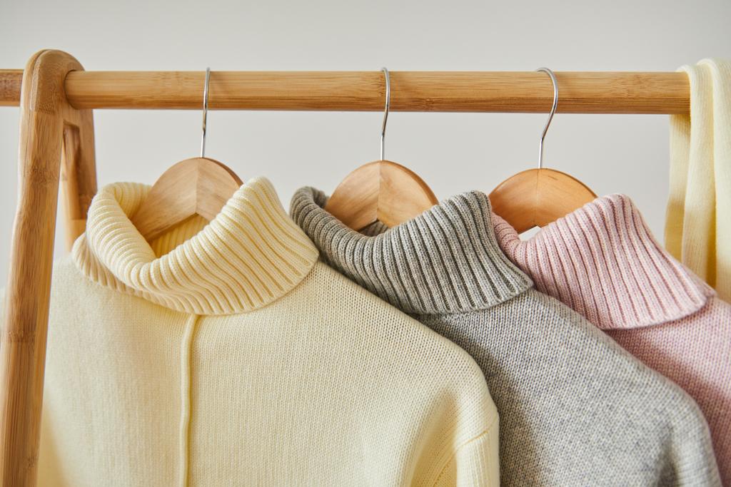 vista de cerca de suéteres suaves de punto rosa, beige y gris colgando en un estante de madera aislado en blanco
 - Foto, imagen
