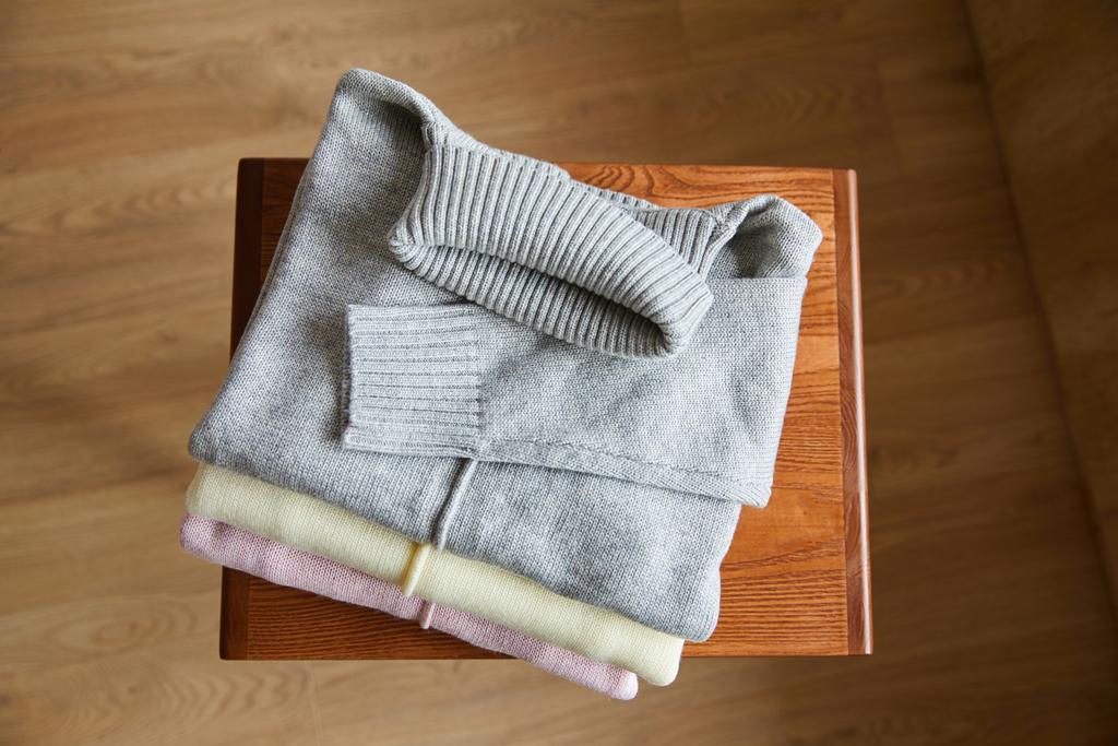 vista superior de suéteres suaves de punto rosa, beige y gris sobre mesa de madera en la habitación
 - Foto, imagen