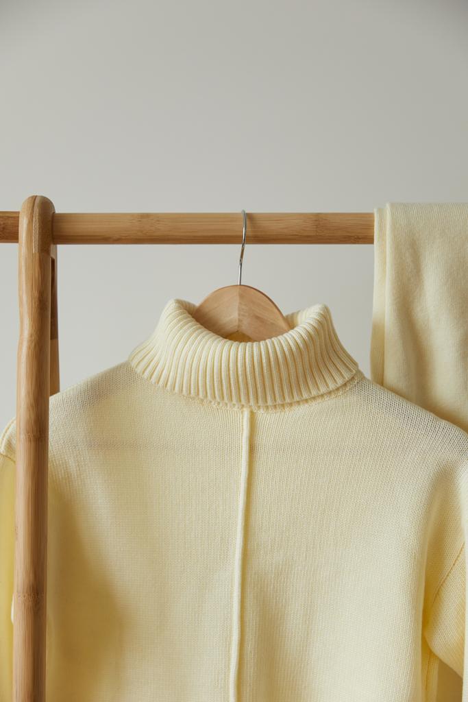 vista de perto de camisola macia de malha bege e calças penduradas no cabide de madeira isolado no branco
 - Foto, Imagem