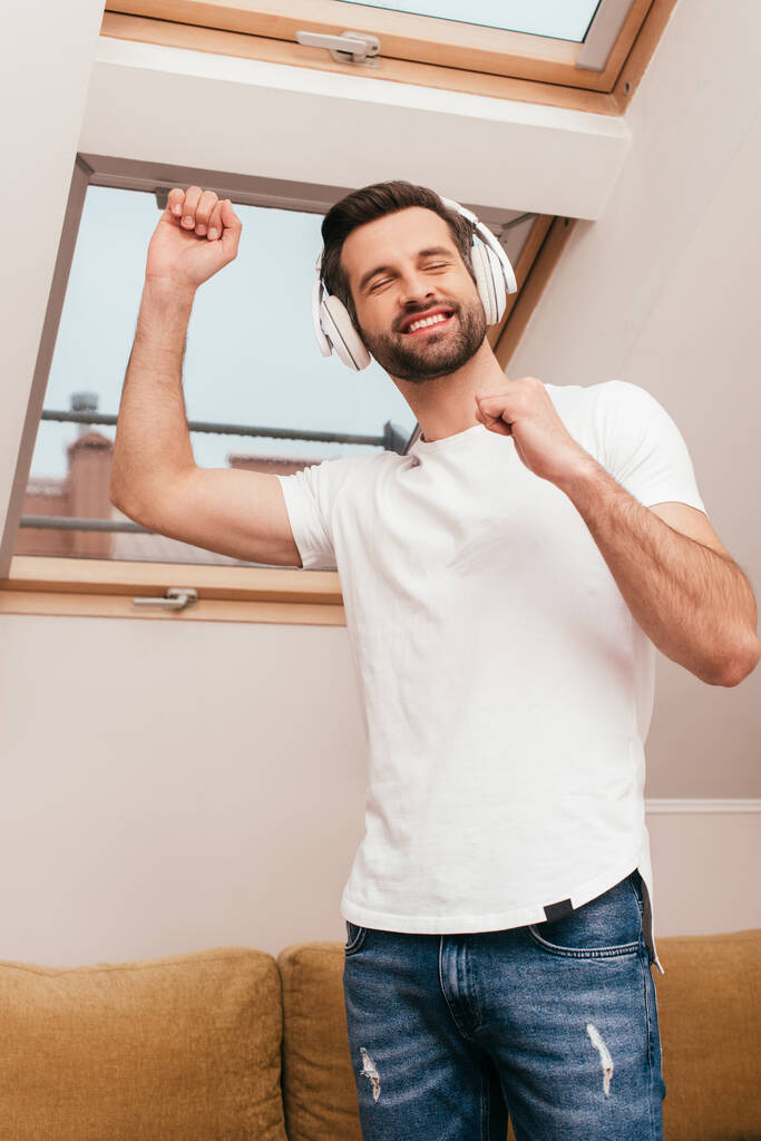 Fröhlicher Mann tanzt, während er zu Hause Musik über Kopfhörer hört  - Foto, Bild