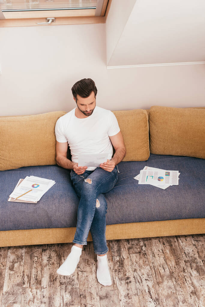 Schöner Mann arbeitet mit Papieren auf Couch zu Hause  - Foto, Bild