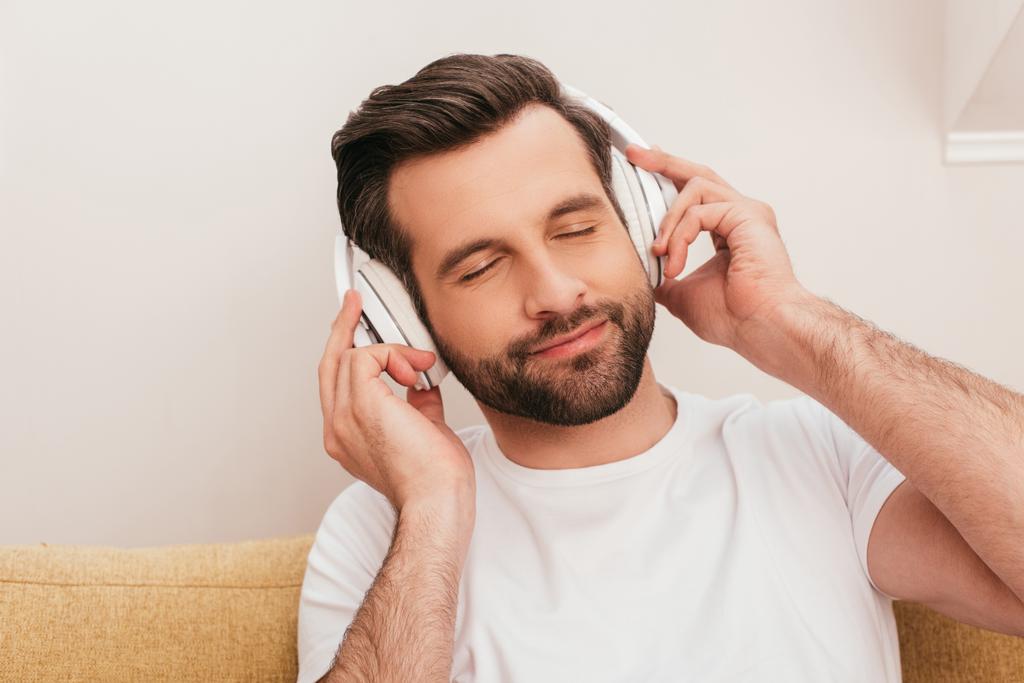 Hombre guapo con los ojos cerrados escuchando música en los auriculares en casa
  - Foto, imagen
