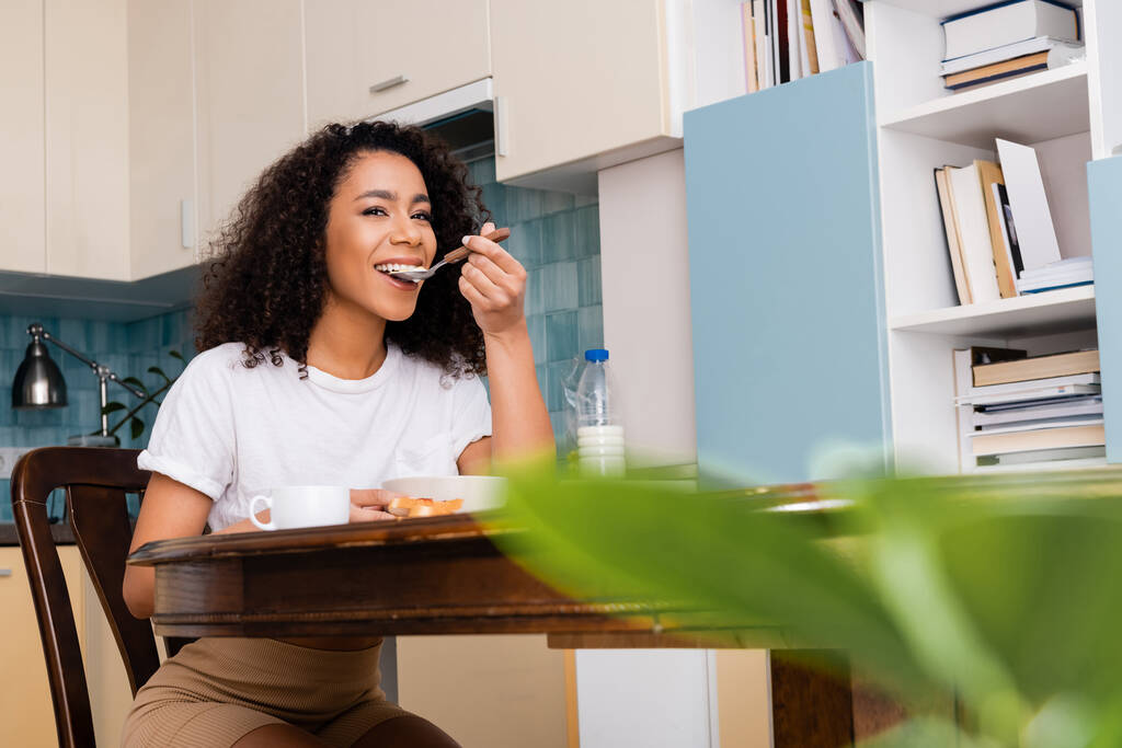 happy african american woman eating tasty breakfast near cup of coffee - Photo, Image