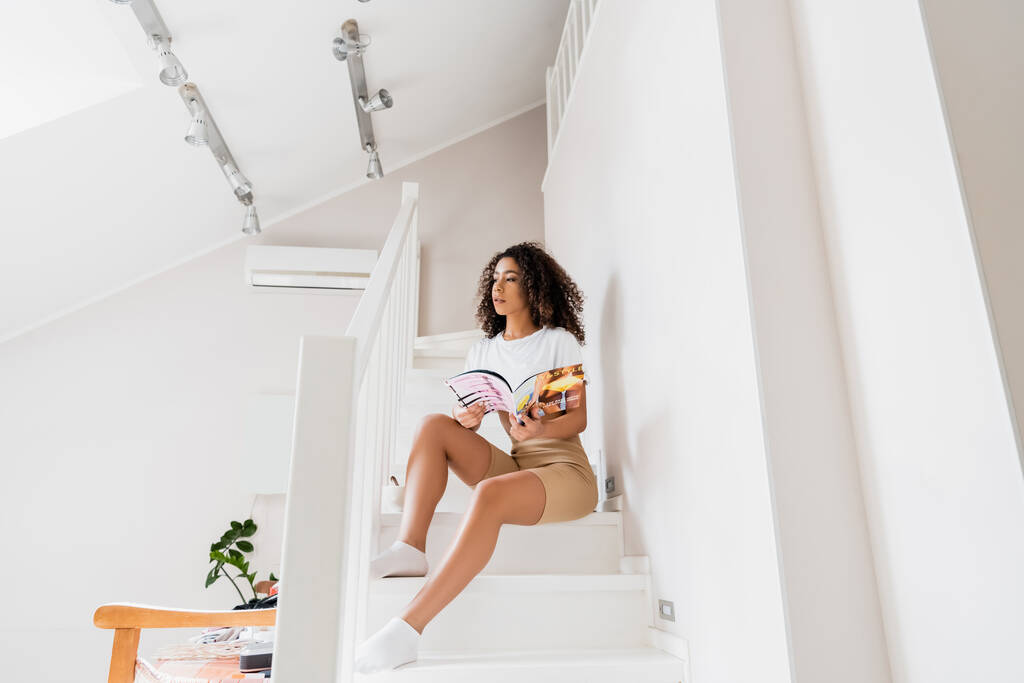 jong Afrikaans amerikaans vrouw zitten op trap met tijdschrift  - Foto, afbeelding