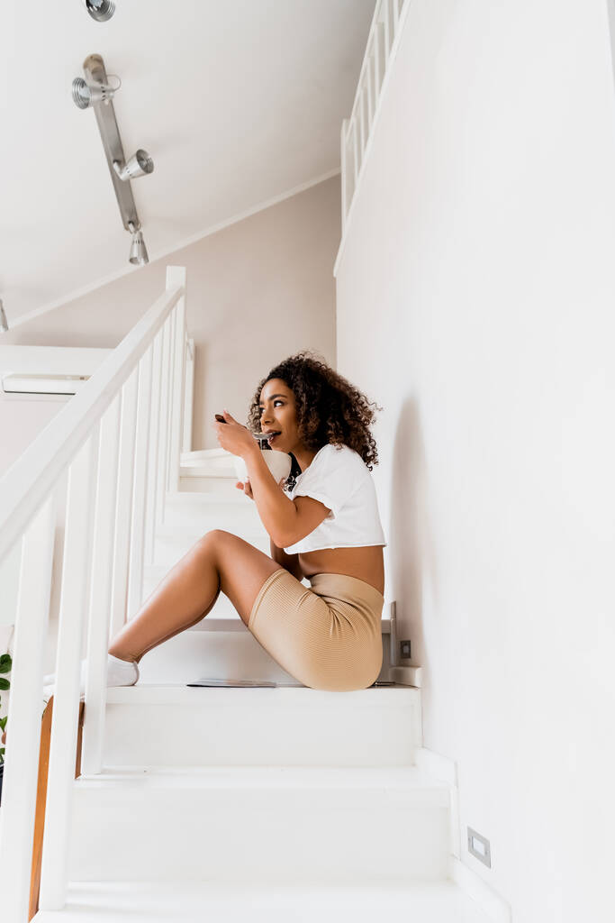 jovem afro-americana sentada nas escadas e tomando café da manhã
  - Foto, Imagem