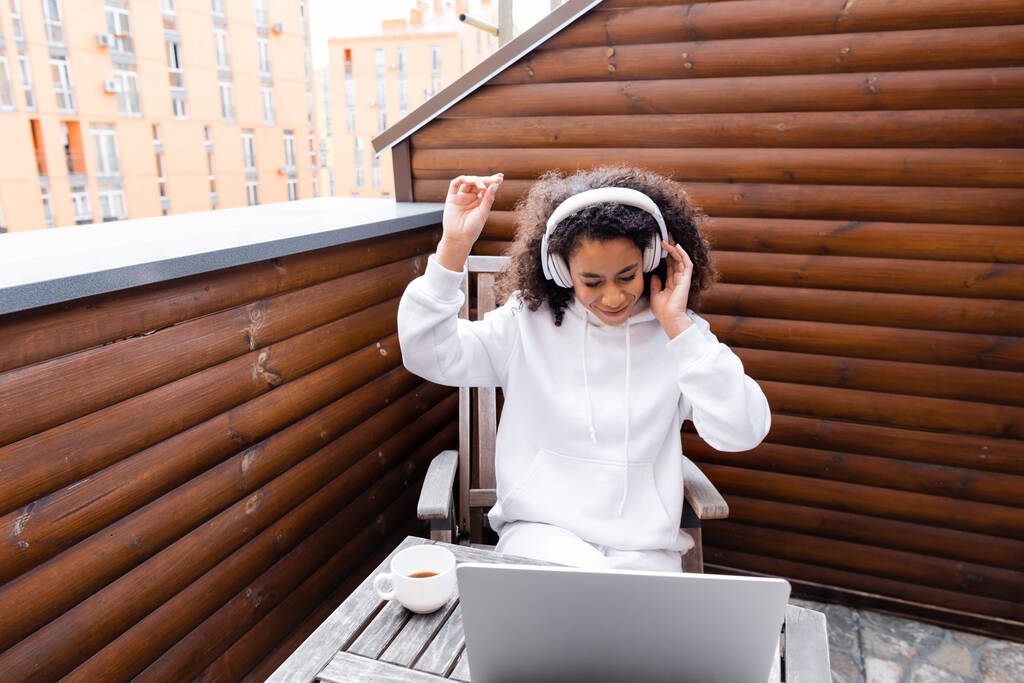 heureux afro-américain pigiste dans les écouteurs sans fil écouter de la musique près d'un ordinateur portable et une tasse de café
  - Photo, image