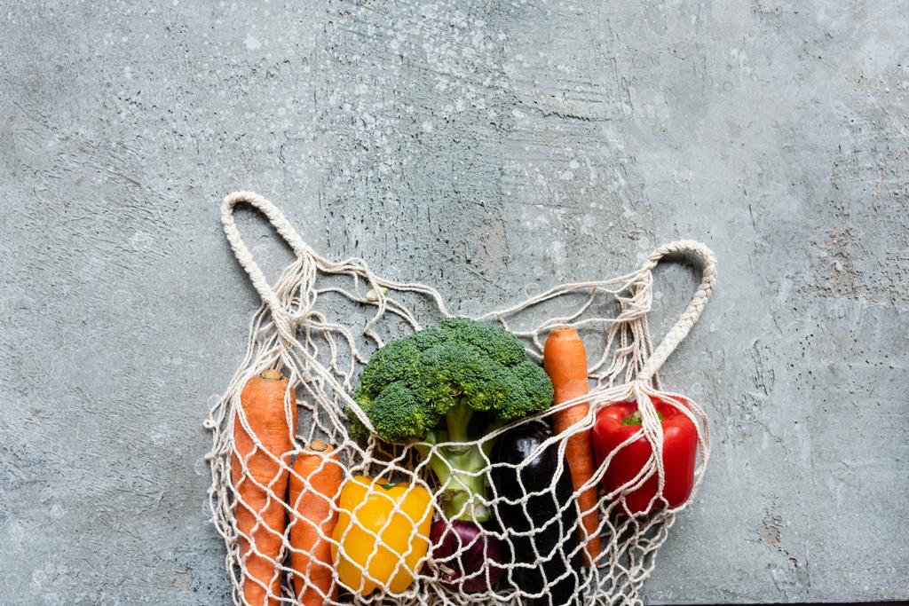 top view of fresh ripe vegetables in string bag on grey concrete surface - Photo, Image