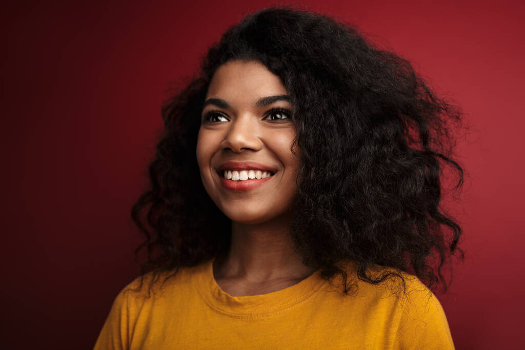 Immagine di una bella donna afroamericana bruna con i capelli ricci che sorride alla telecamera isolata su sfondo rosso
 - Foto, immagini