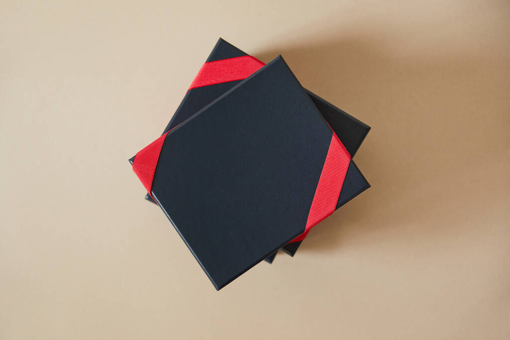 bovenaanzicht van zwarte geschenkdozen met rode linten op beige achtergrond  - Foto, afbeelding