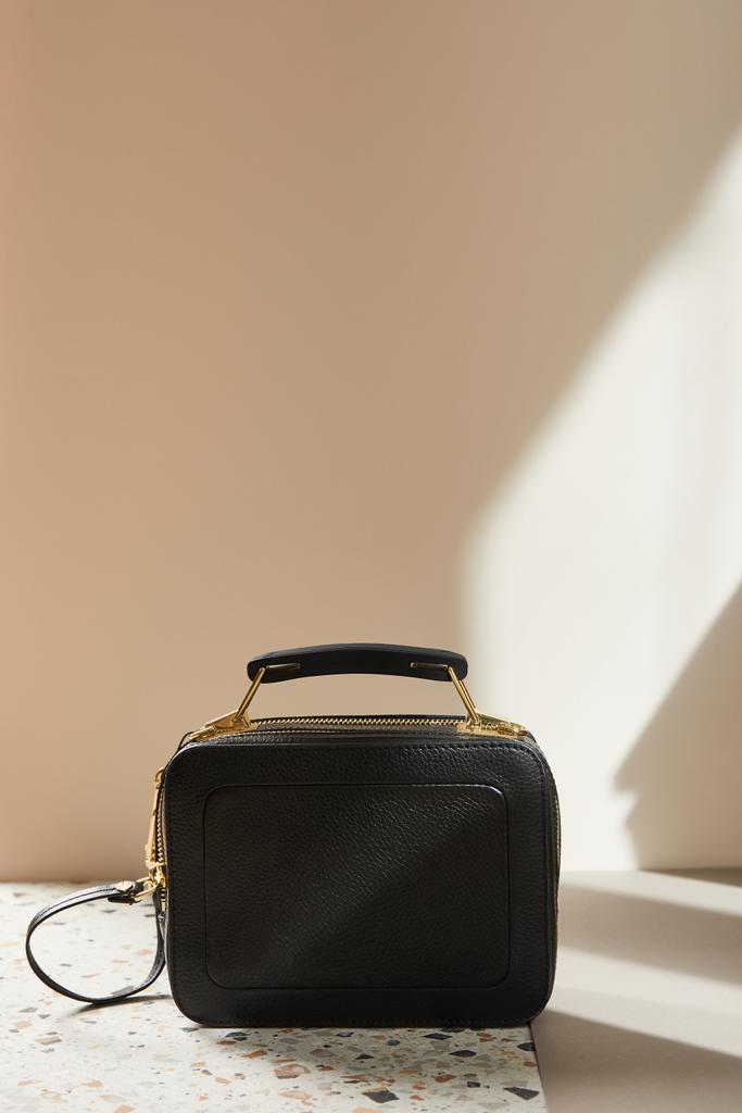 δερμάτινη μαύρη τσάντα με χρυσά φερμουάρ στη μαρμάρινη επιφάνεια σε μπεζ φόντο - Φωτογραφία, εικόνα