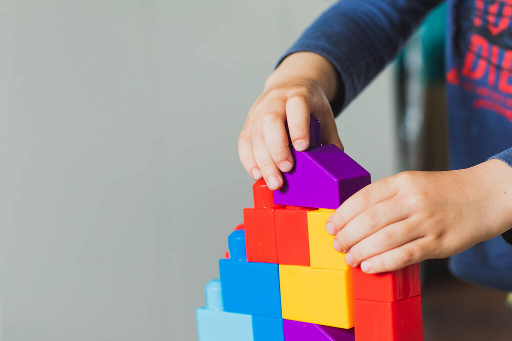 Een jongetje speelt met een kleurrijke bouwer. Constructeur voor kinderontwikkeling. Een kind bouwt een toren van gekleurde blokjes. - Foto, afbeelding