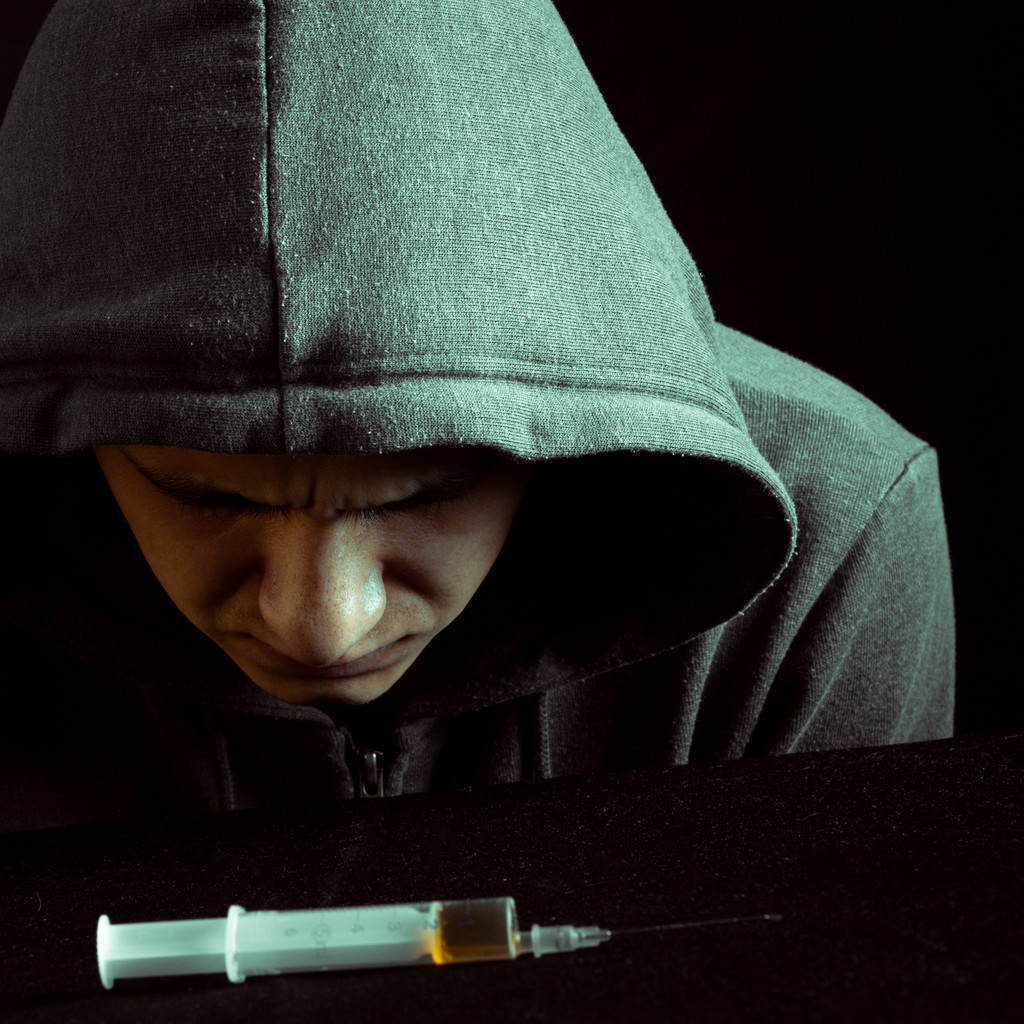 Grunge image of a depressed drug addict looking at a syringe and drugs - Photo, Image