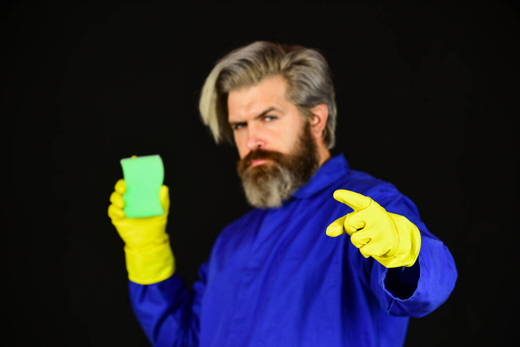 vousatý muž ve žlutých gumových rukavicích, otírající prach prachem. doma uklízet. Koncept úklidu. Povinnost a čistota. samec používající houbu. Dávej pozor na hygienu. Vousatý muž s čistícím vybavením - Fotografie, Obrázek