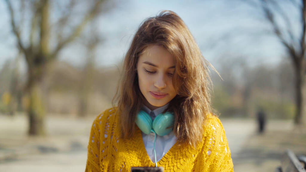 Jeune fille avec écouteurs utilisant le téléphone dans un parc de la ville. - Photo, image