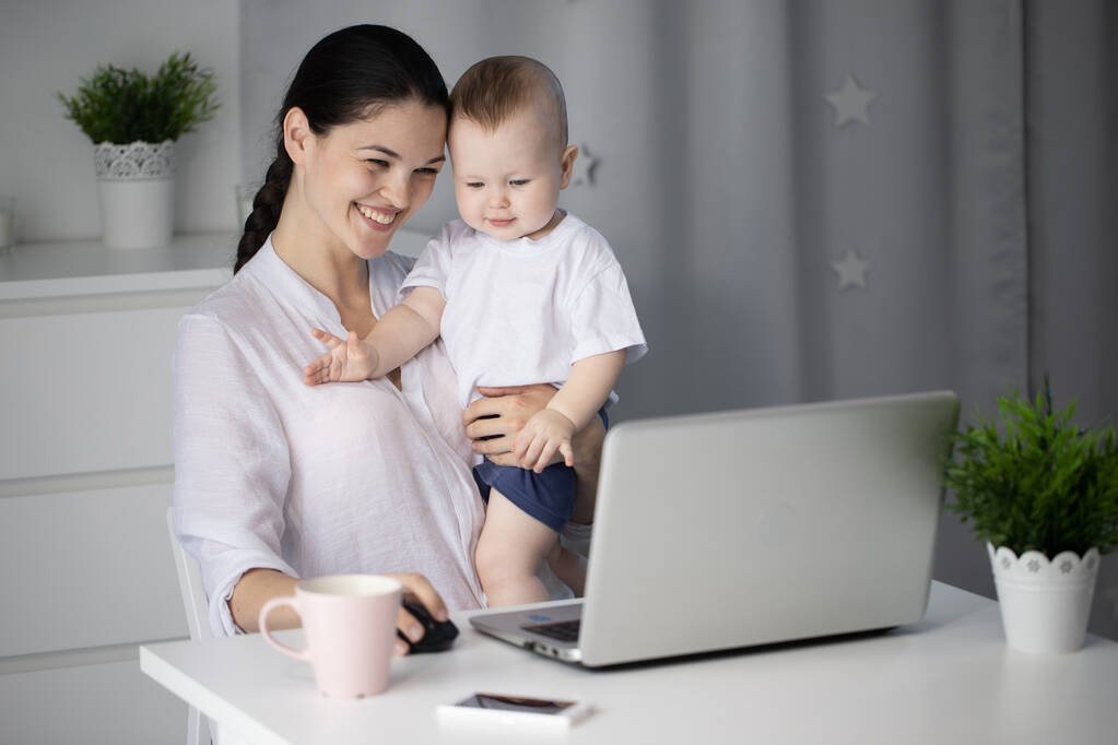 Молодая мать работает в указе за компьютером с маленьким сыном на руках
 - Фото, изображение