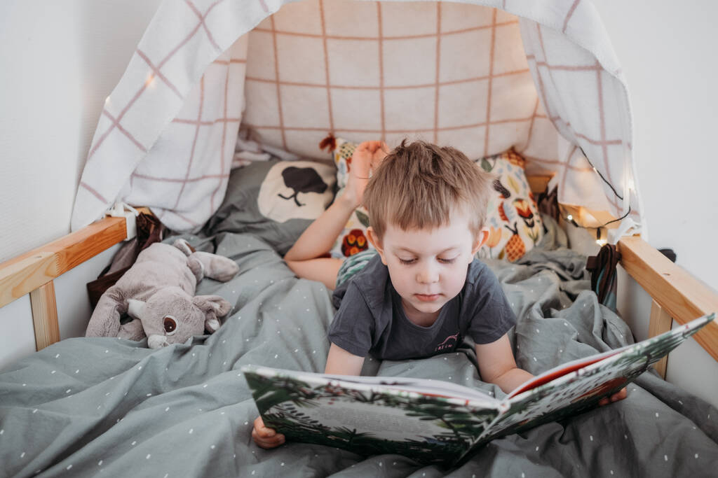 óvodás fiú könyvet olvas az ágyában. eltölteni egy kis időt otthon. Életmód családi koncepció - Fotó, kép