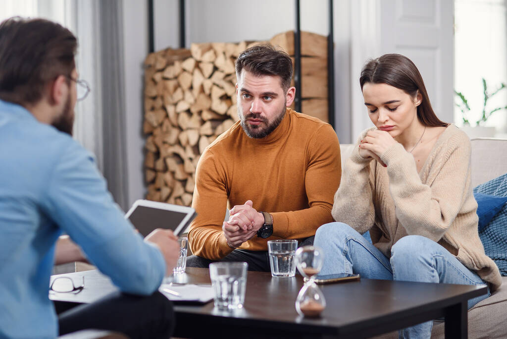 Ενοχλημένο καυκάσιο ζευγάρι αντρών και γυναικών συζητούν με ψυχολόγο σε συνεδρία θεραπείας στο light room. - Φωτογραφία, εικόνα