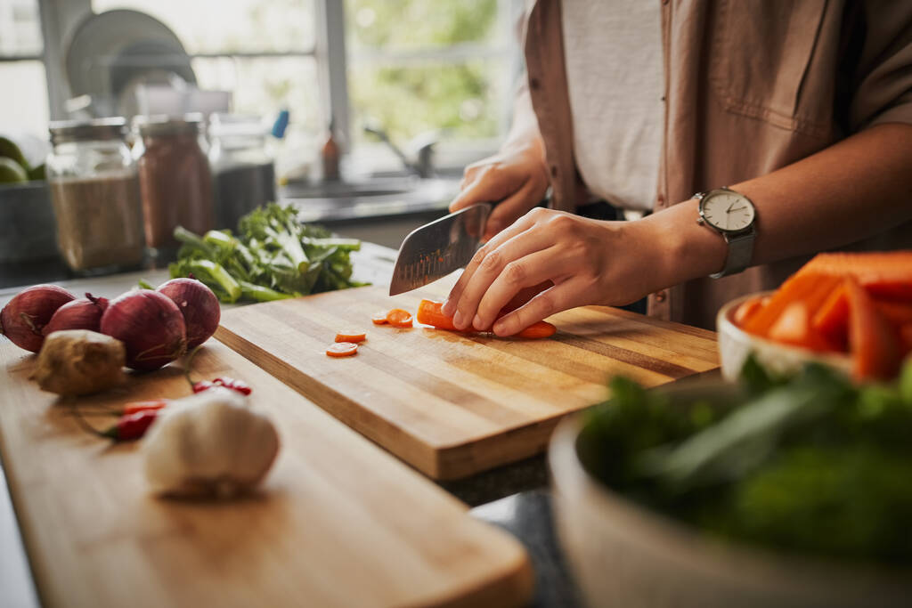 Szoros női kéz vágás friss narancs sárgarépa a fedélzeten, míg a modern konyhában - egészséges élelmiszer, hogy fokozza az immunrendszert  - Fotó, kép