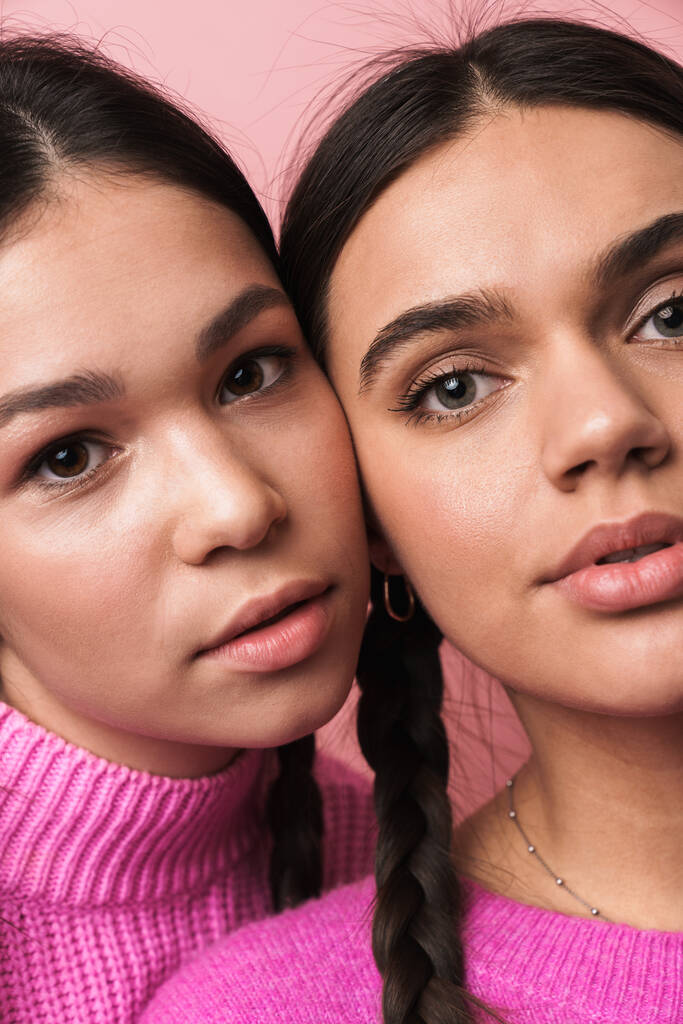 Изображение двух привлекательных девочек-подростков с косичками в повседневной одежде, смотрящих на камеру на розовом фоне
 - Фото, изображение