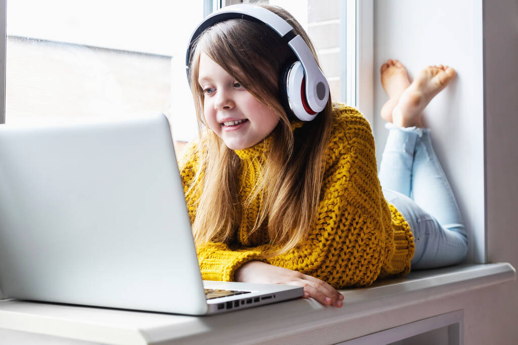 自宅の女の子はインターネット上の友人と通信します。子供の距離学習。自宅でノートパソコンを使ってかわいい女の子。教育、オンライン研究、家庭学習、女子学生のライフスタイルの概念 - 写真・画像