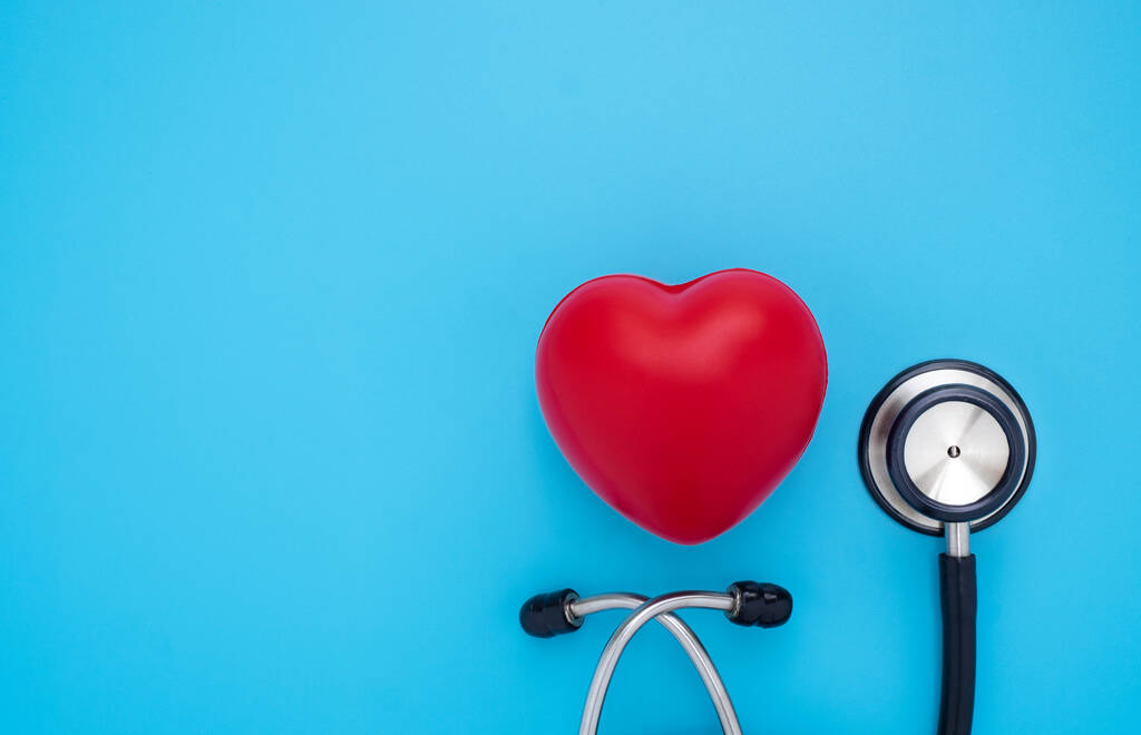 青い背景の検査のための医師の赤い心臓と黒の聴診器のクローズアップ。音を診断するための医療用聴診器。コピーとヘルスケアと心臓学の概念  - 写真・画像