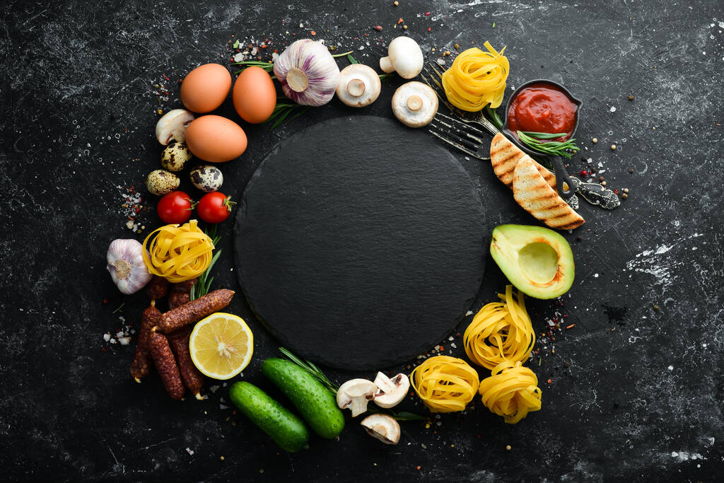 Conjunto de alimentos saludables: tomates, pasta, especias, verduras y embutidos. Vista superior. Fondo de piedra negra
. - Foto, Imagen