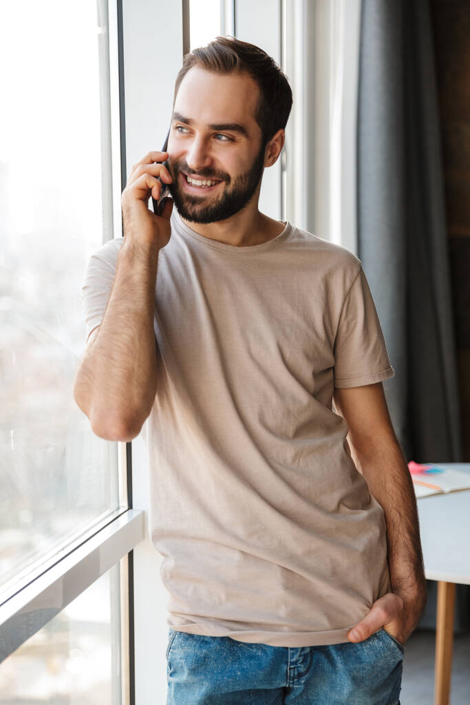 Imagen de un joven sonriente y positivo en casa hablando por teléfono móvil
. - Foto, imagen