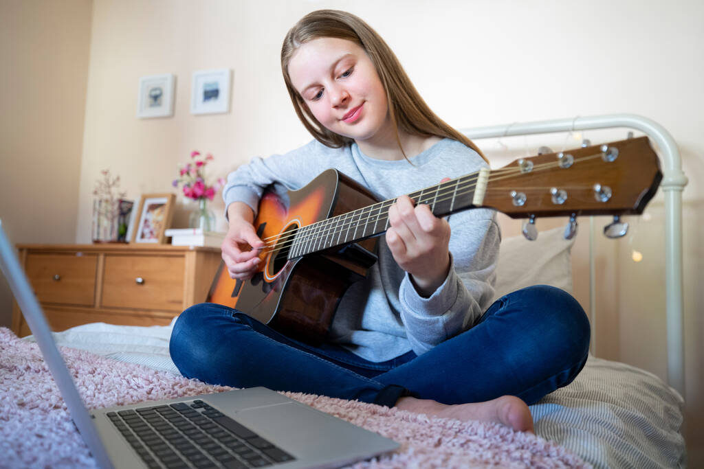 Teenage Girl Learning To Play Acosutic Guitar Mit Online-Unterricht am Laptop-Computer - Foto, Bild