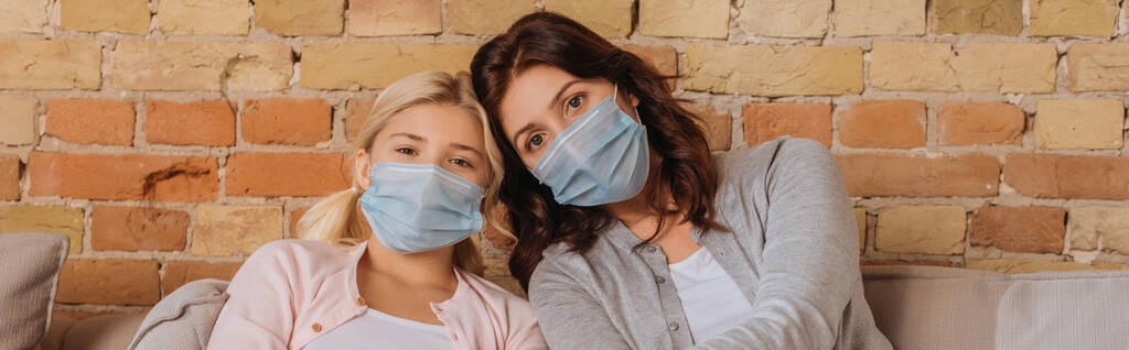 Mother and daughter in medical masks looking at camera at home  - Photo, Image