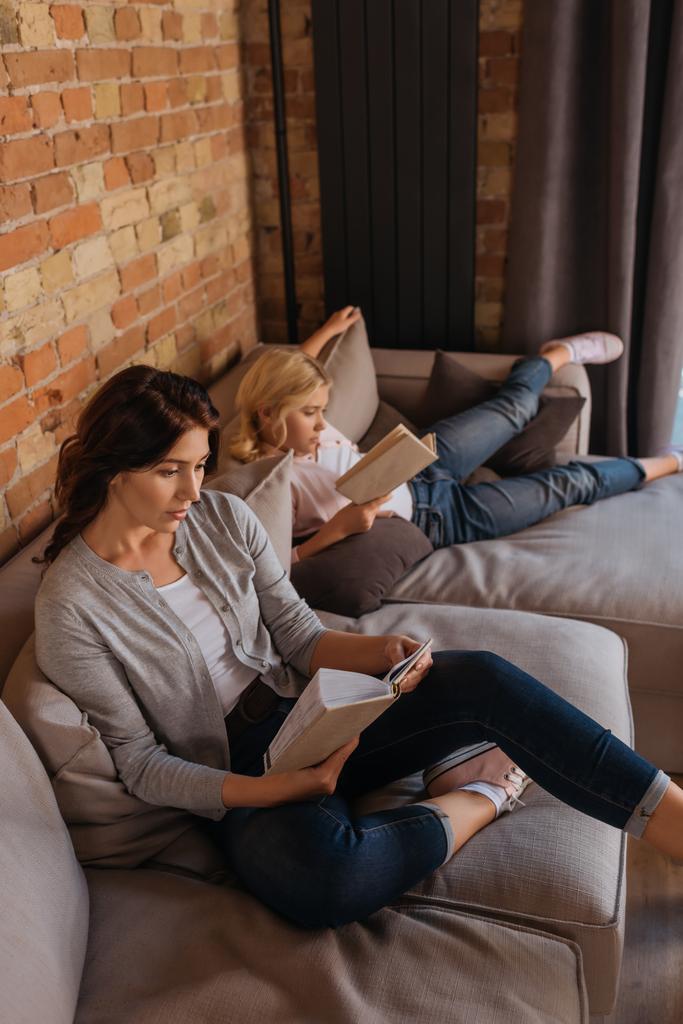 Мать и дочь читают книги, сидя дома на диване
  - Фото, изображение