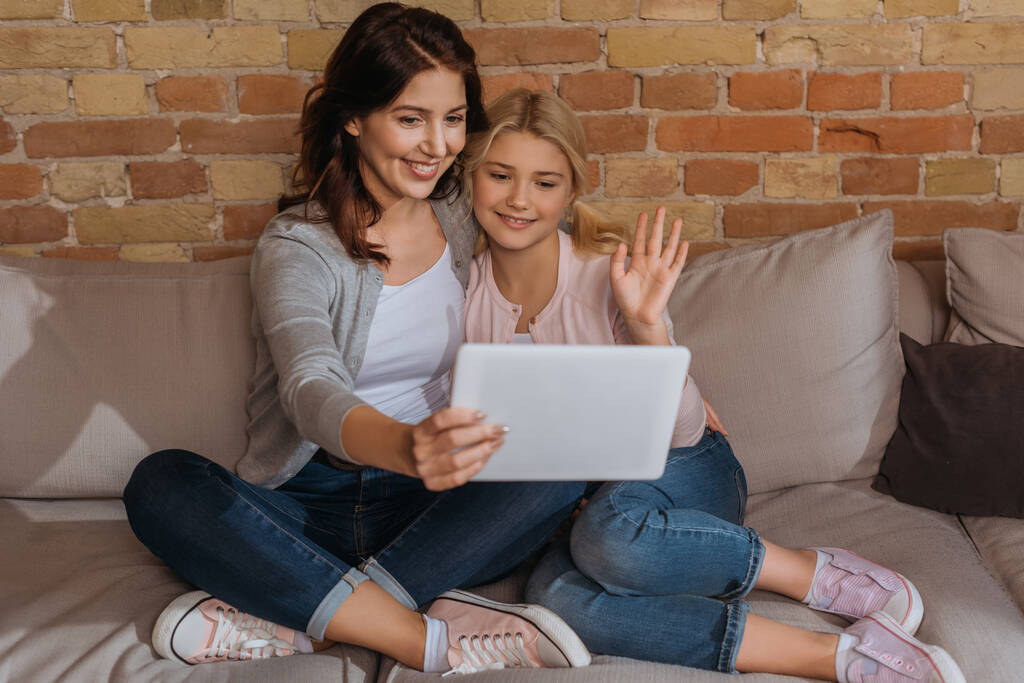 Вибірковий фокус усміхненої дитини і матері, що має відеодзвінок на цифровому планшеті на дивані
  - Фото, зображення