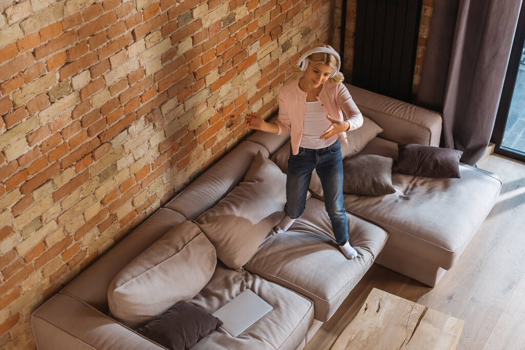 Yleisnäkymä lapsi kuulokkeet seisoo sohvalla kotona
  - Valokuva, kuva