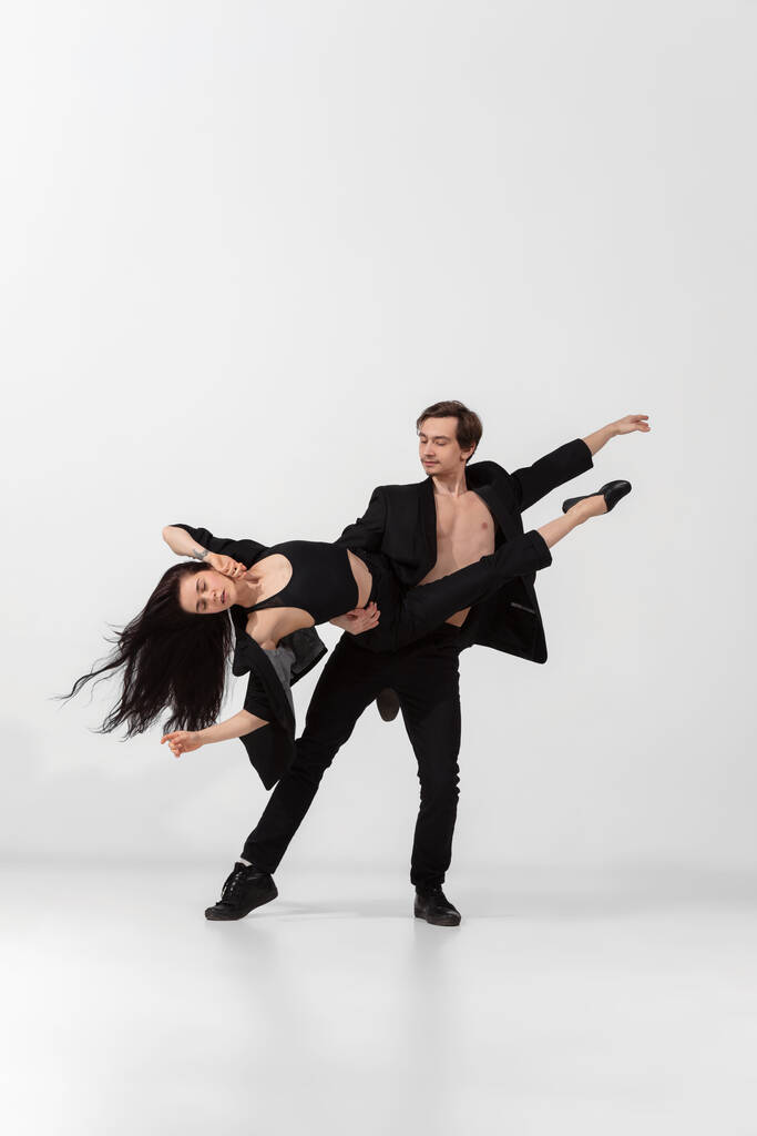 Junge und anmutige Balletttänzer in minimalem schwarzen Stil isoliert auf weißem Studiohintergrund - Foto, Bild