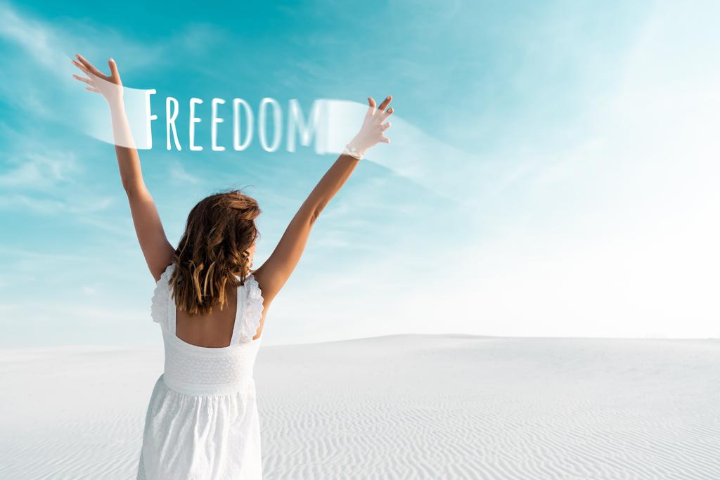 back view of beautiful girl in white dress with hands in air on sandy beach with blue sky, freedom illustration - Photo, Image