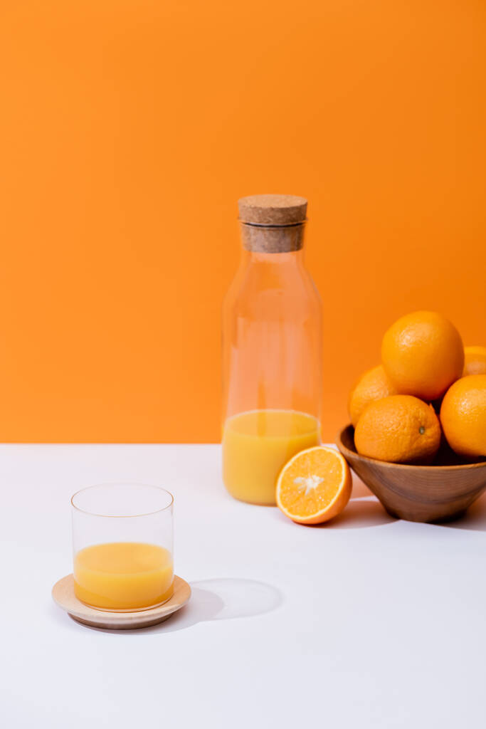 zumo de naranja fresco en vidrio y botella cerca de naranjas en tazón sobre superficie blanca aislado en naranja
 - Foto, Imagen