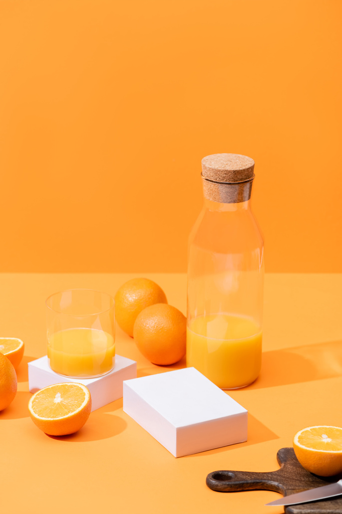 熟したオレンジの近くのガラスとボトルの新鮮なオレンジジュース、オレンジに孤立したナイフで木製のまな板 - 写真・画像
