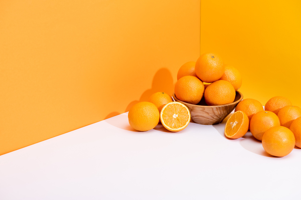 свежие апельсины в миске на белой поверхности на оранжевом фоне
 - Фото, изображение