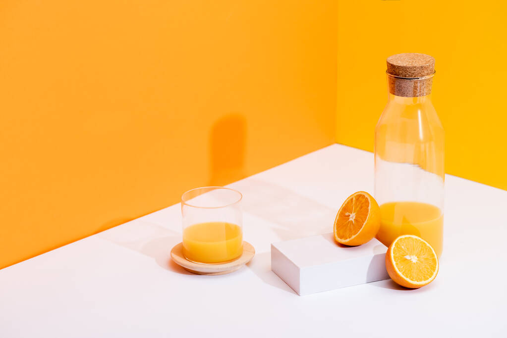 čerstvý pomerančový džus ve skle a láhvi u zralých pomerančů na bílém povrchu na oranžovém pozadí - Fotografie, Obrázek