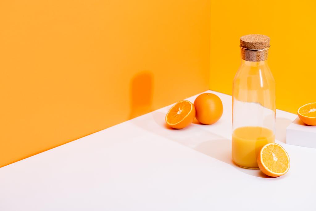 zumo de naranja fresco en botella de vidrio cerca de naranjas maduras en la superficie blanca sobre fondo naranja
 - Foto, imagen