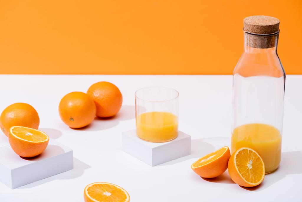 čerstvý pomerančový džus ve skle a láhvi u zralých pomerančů na bílém povrchu izolované na oranžové - Fotografie, Obrázek