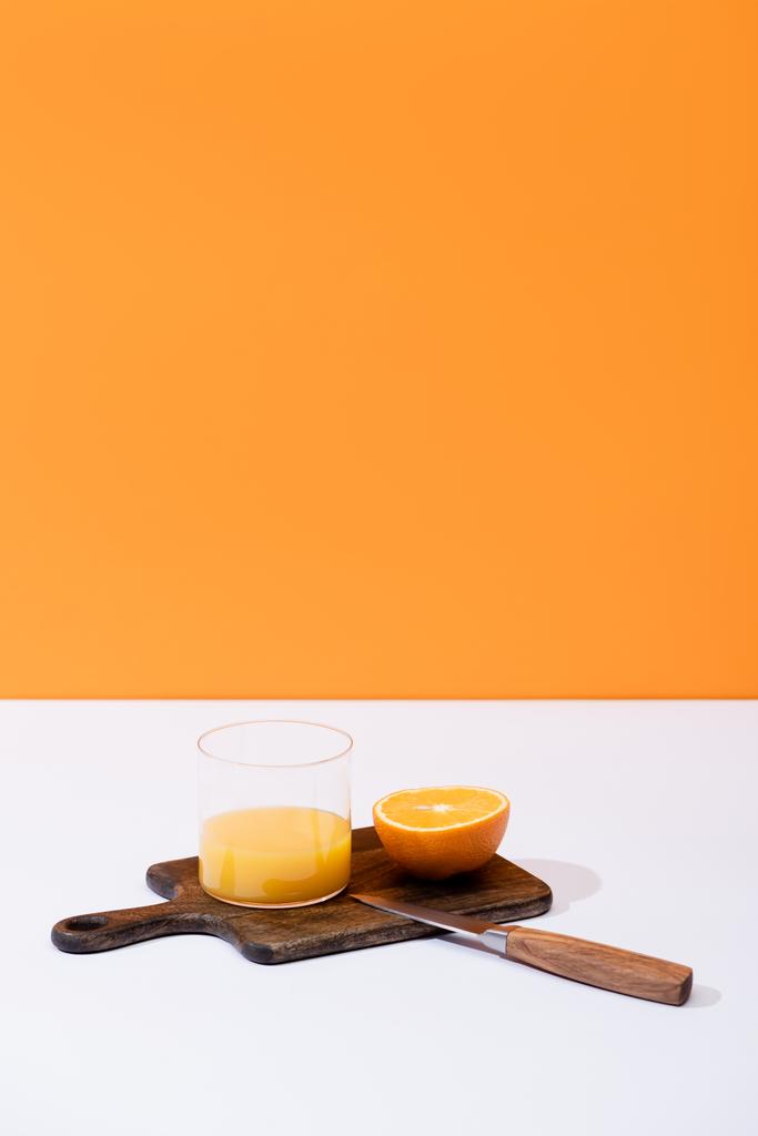 свіжий апельсиновий сік у склянці біля розрізаних фруктів на дерев'яній обробній дошці з ножем на білій поверхні ізольовані на апельсині
 - Фото, зображення