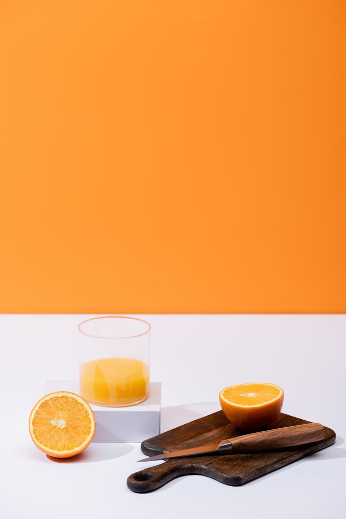 suco de laranja fresco em vidro perto de frutas cortadas em tábua de corte de madeira com faca na superfície branca isolada em laranja
 - Foto, Imagem