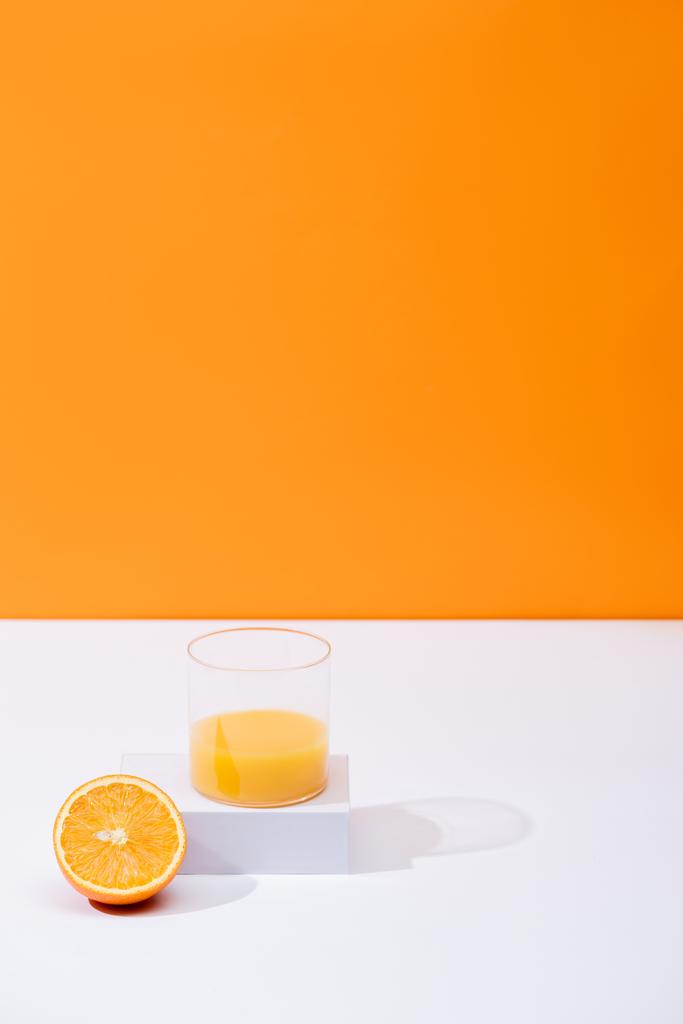 Portakalda izole edilmiş beyaz yüzeyde kesilmiş meyvenin yanında cam içinde taze portakal suyu. - Fotoğraf, Görsel
