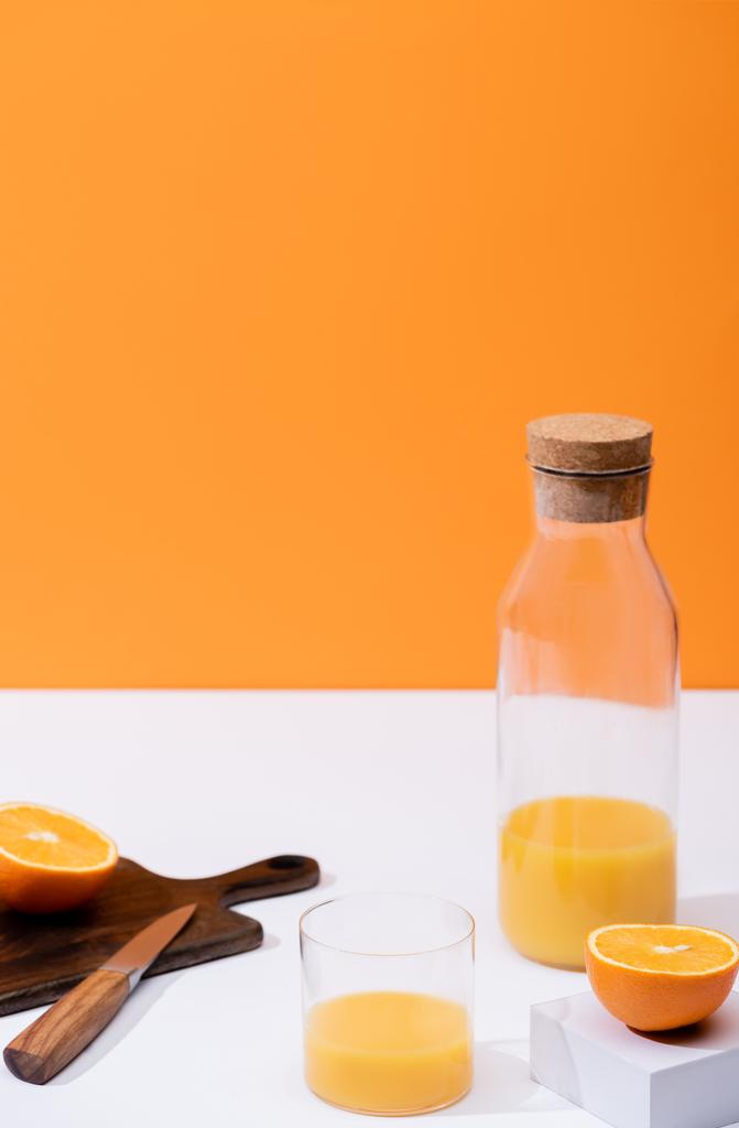 suco de laranja fresco em vidro e garrafa perto de frutas cortadas em tábua de corte de madeira com faca na superfície branca isolada em laranja
 - Foto, Imagem