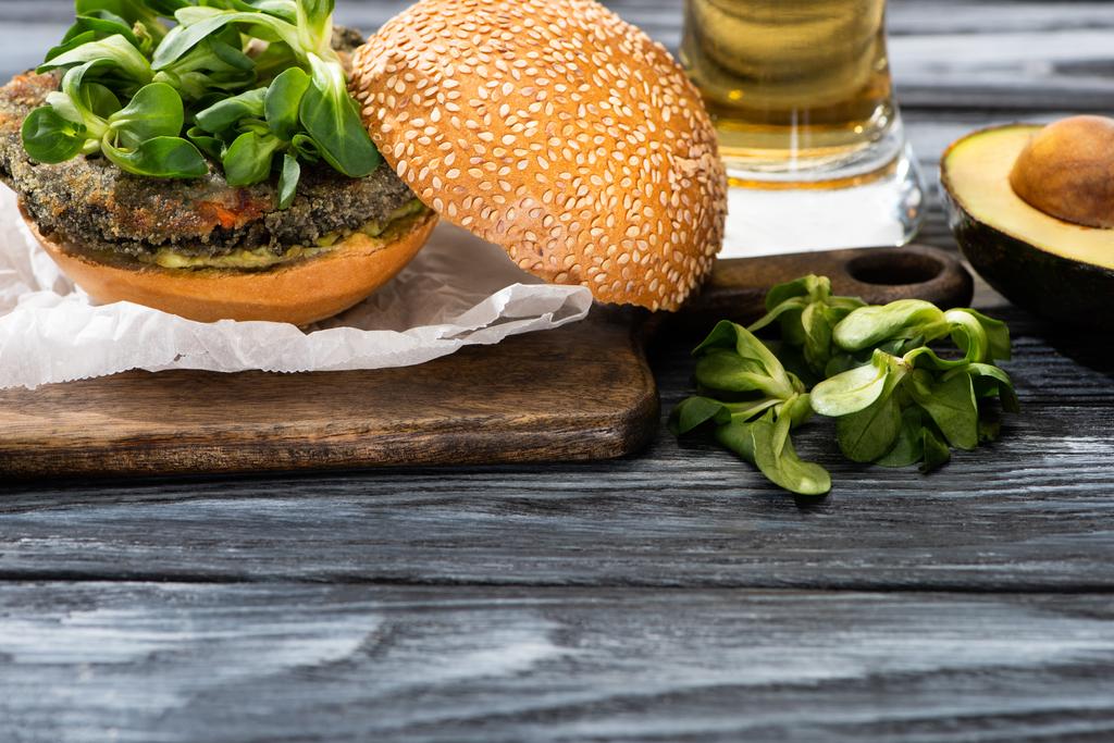 lekkere veganistische hamburger met microgreens geserveerd op snijplank bij avocado en bier op houten tafel - Foto, afbeelding