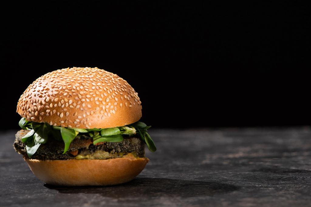 sabrosa hamburguesa vegana con microgreens servidos en superficie texturizada aislado en negro
 - Foto, imagen