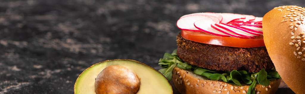 hambúrguer vegan saboroso com legumes servidos com abacate metade na superfície texturizada, cultura panorâmica
 - Foto, Imagem