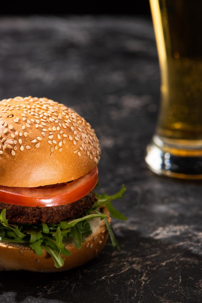 selektiver Schwerpunkt des leckeren veganen Burgers mit Tomaten und Gemüse, serviert auf strukturierter Oberfläche mit Bier - Foto, Bild