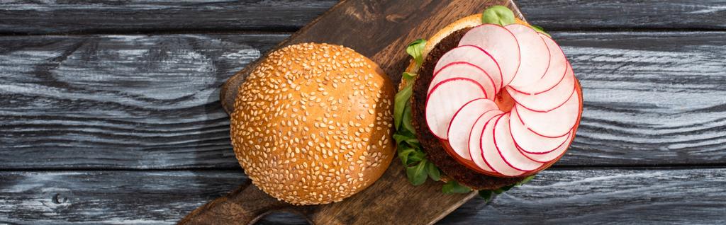 vrchní pohled na chutný veganský burger s mikrozelení, ředkvička, rajče na řezací desce servírované na dřevěném stole, panoramatická plodina - Fotografie, Obrázek