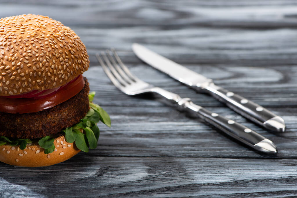 selective focus of tasty vegan burger with vegetables served on wooden table with fork and knife - Photo, Image